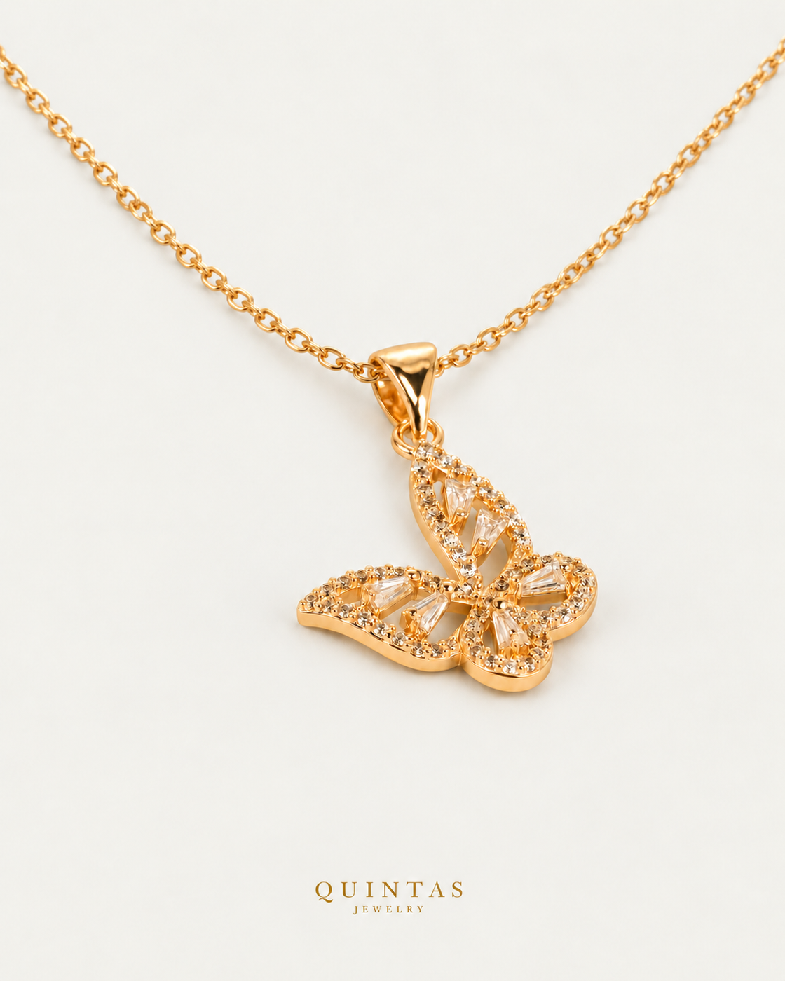 Alora Grand Butterfly Necklace — gold cable chain, genuine oblique detail, neutral greige background; canonical Quintas Jewelry logo
