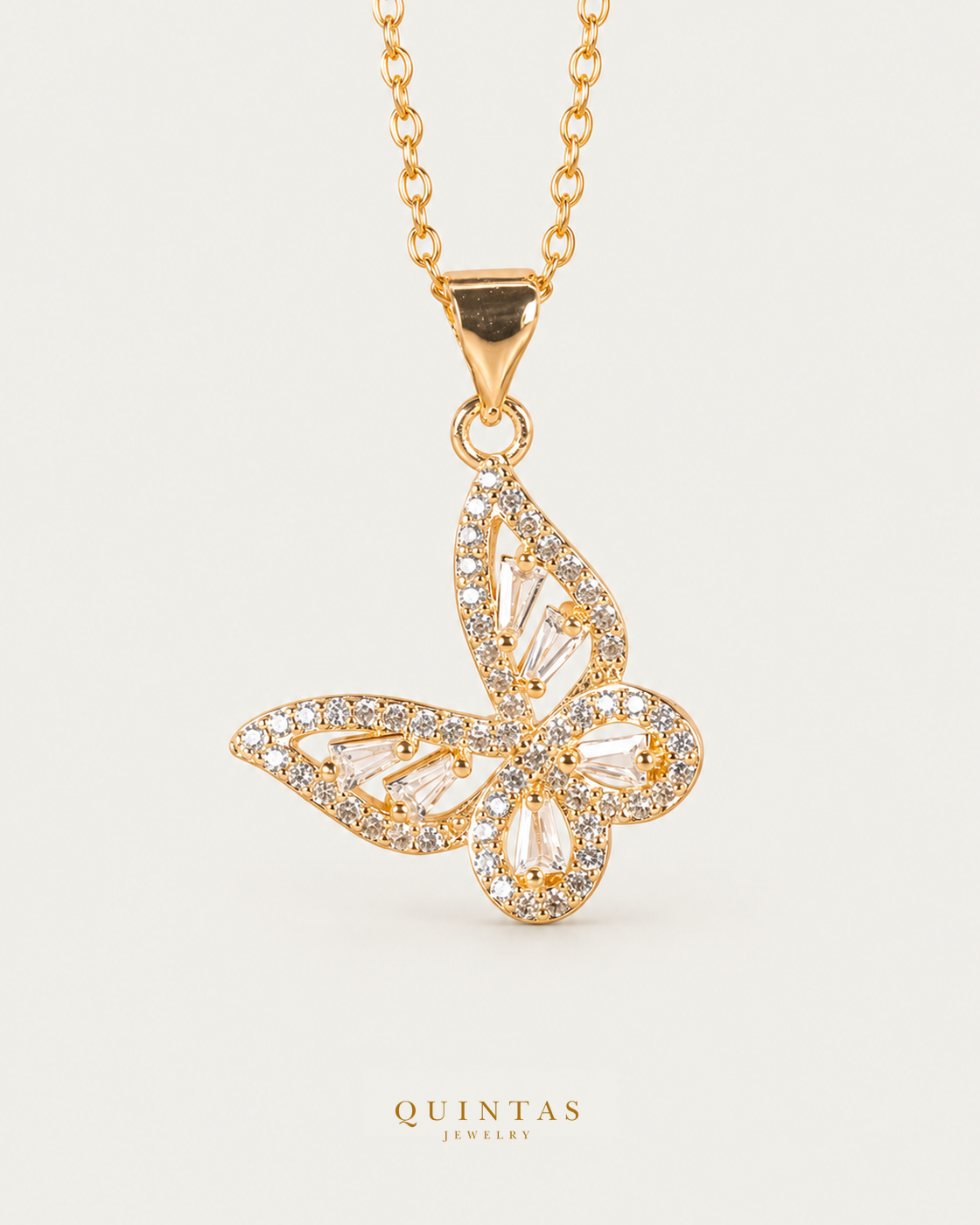Alora Grand Butterfly Necklace — gold cable chain, front hero, neutral greige background; canonical Quintas Jewelry logo