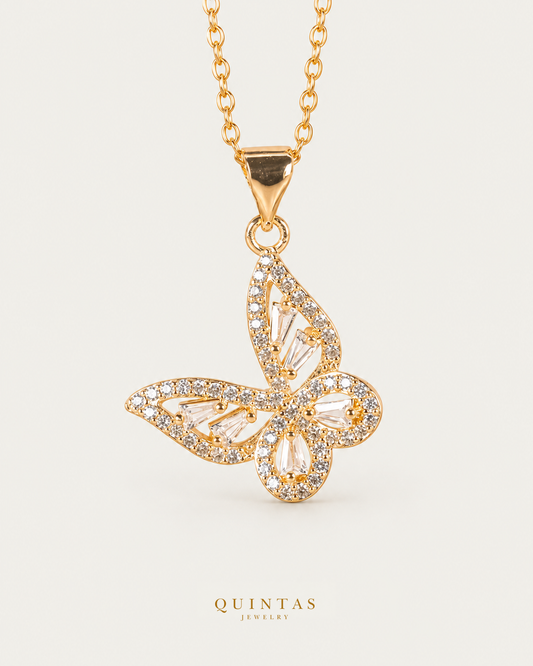 Alora Grand Butterfly Necklace — gold cable chain, front hero, neutral greige background; canonical Quintas Jewelry logo