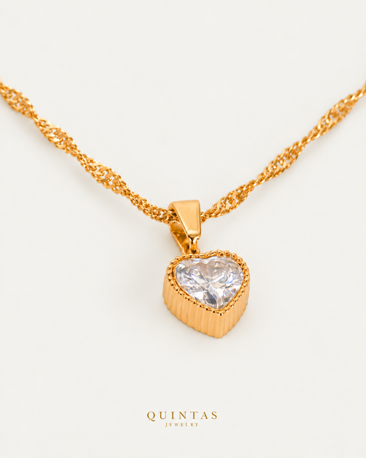 Adeline Crystal Heart Necklace — source-verified Singapore oblique view, off-white background, canonical gold logo
