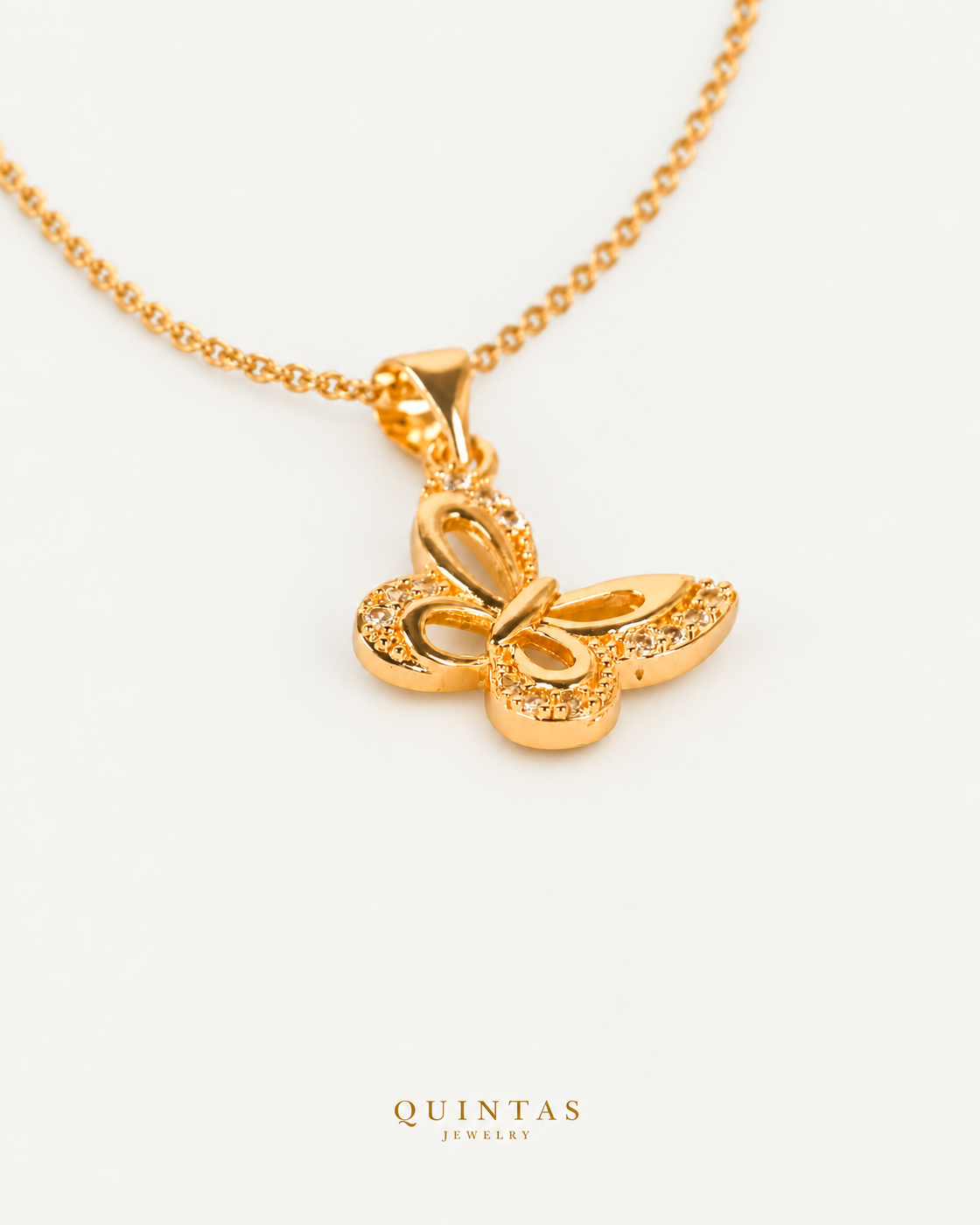 Marinella Butterfly Necklace — gold cable, genuine oblique angle, neutral greige; canonical Quintas Jewelry logo