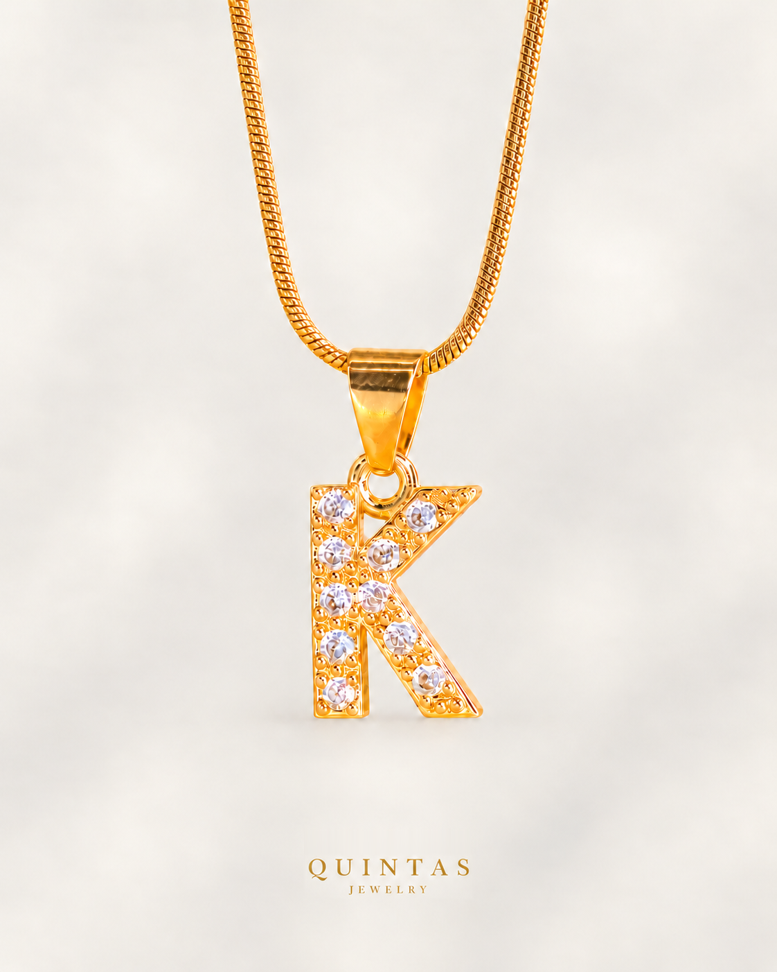 QUINTAS Zirconia Letter Initial Necklace — K on off-white background